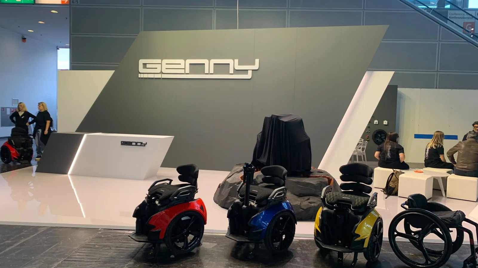 Genny-Mobility-Messestand auf der REHACARE 2026 mit drei Genny-Zero-Modellen, einer verhüllten Genny Zero XR und Besuchern