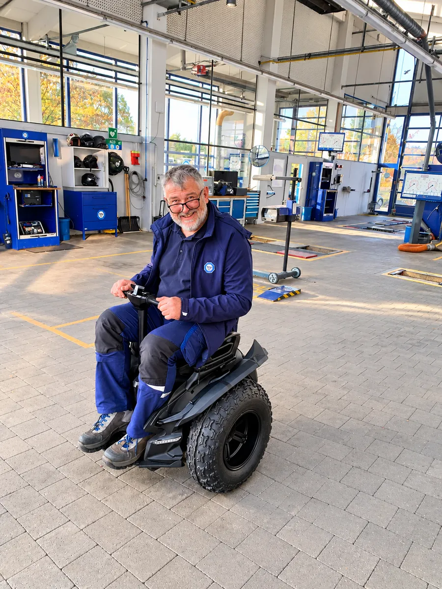 Lächelnder Mann in blauer Arbeitsjacke sitzt in der Prüfhalle auf der Genny Zero XR mit Offroad-Bereifung